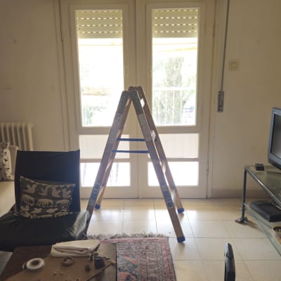 סולם עץ מוצב מול חלון וארגז תריס גלילה במהלך תיקון