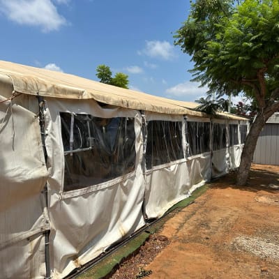 אוהל לבן עם חלונות פלסטיק ועץ לידו