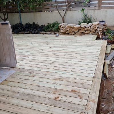 דק עץ חדש בגינה עם ערימת אבנים בצד