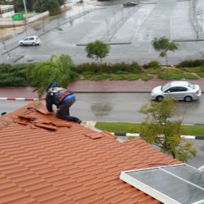 אדם מתקן רעפים על גג רעפים אדום