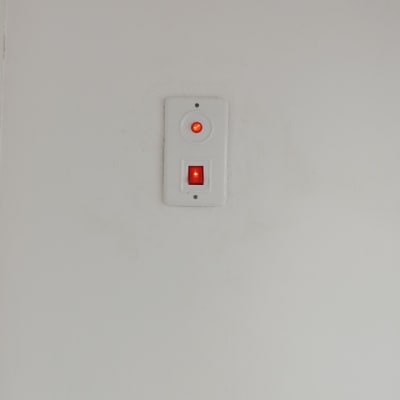 מתג דולק עם נורית חיווי אדומה על קיר לבן