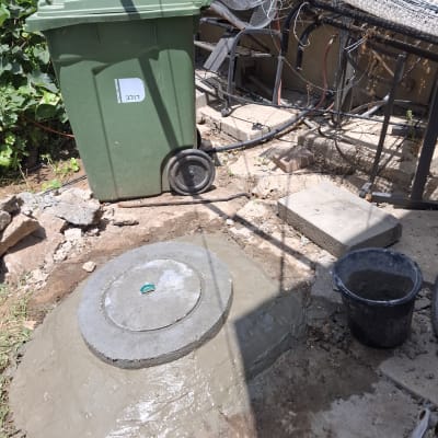 מכסה בטון עגול על הקרקע ליד פח ירוק