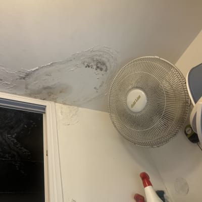 כתם רטיבות בתקרה ליד מאוורר וקיר עם חלון