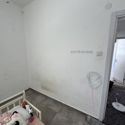 קיר עם כתמי צבע וציורים, מיטה וצעצועים בחדר ילדים