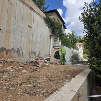 אדם בחליפת עבודה ירוקה מנקה אזור חיצוני ליד קיר בטון