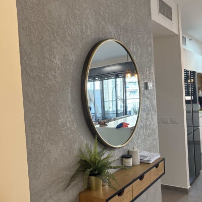 קיר צבוע עם מראה עגולה ומדף עץ עם צמח.