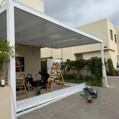 התקנת פרגולה אלומיניום בחצר בית עם סולמות וכלים