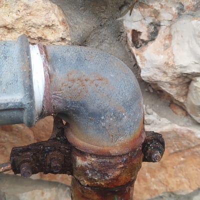 צינור מתכת חלוד עם חיבור זוויתי על קיר אבן