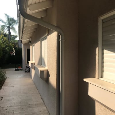 מרזב מתכת מחובר לגג בית עם רעפים לבנים