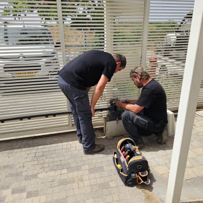 שני אנשים מתקנים שער חשמלי עם כלי עבודה