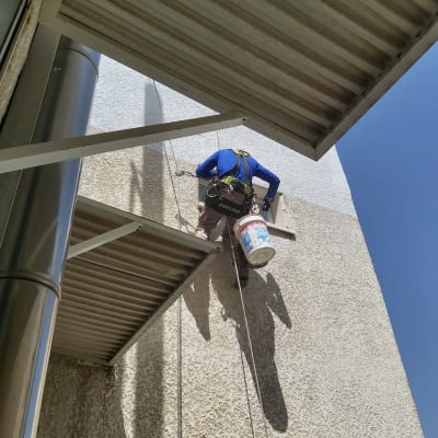 אדם תלוי על חבלים צובע קיר חיצוני