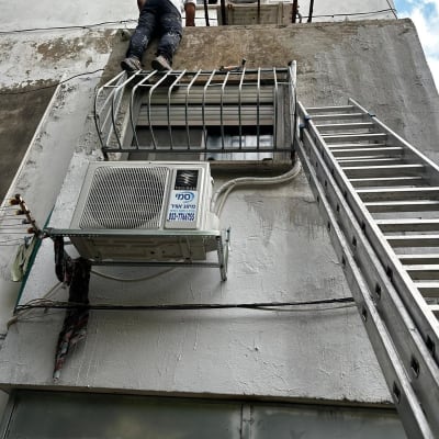 אדם על סולם ליד מזגן מותקן על קיר חיצוני