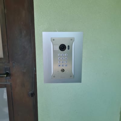 אינטרקום עם מצלמה ולוח מקשים על קיר ירוק