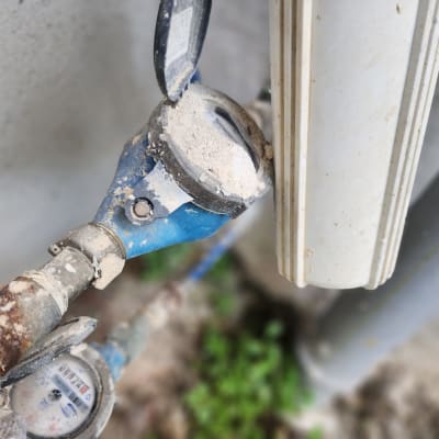 מד מים כחול עם מכסה פתוח וצינור חלוד