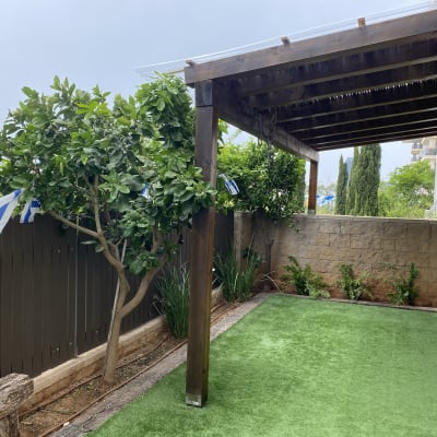 פרגולה מעץ בגינה עם דשא סינתטי ועצים