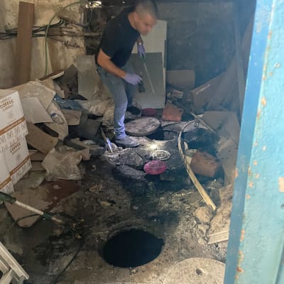 אדם עם כפפות ליד בור פתוח בחדר מבולגן