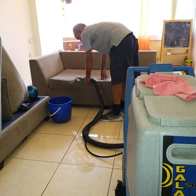 אדם מנקה ספה עם מכונת ניקוי ושואב אבק