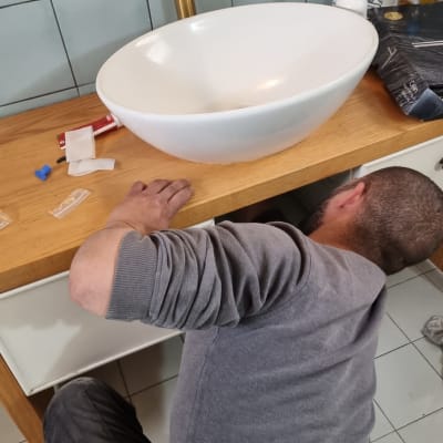 אדם מתקן צנרת מתחת לכיור בחדר אמבטיה