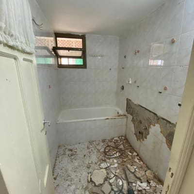 חדר אמבטיה בשיפוץ עם קיר שבור וכלים על הרצפה