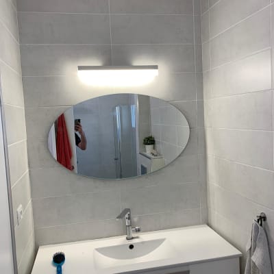 מראה אובלית תלויה על קיר בחדר אמבטיה