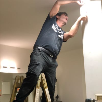 חשמלאי עובד על תקרה בעזרת סולם וכלי עבודה