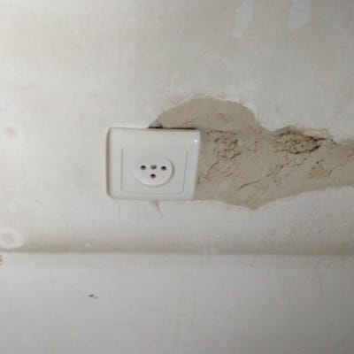 שקע חשמל בקיר עם טיח מתקלף סביבו