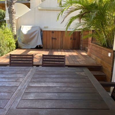 דק עץ עם שולחן וכיסאות, צמחייה ירוקה בצד