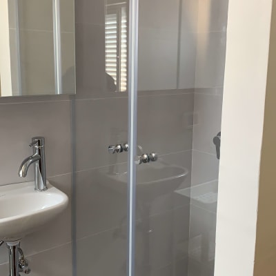 מקלחון זכוכית עם ברזים וכיור לידו