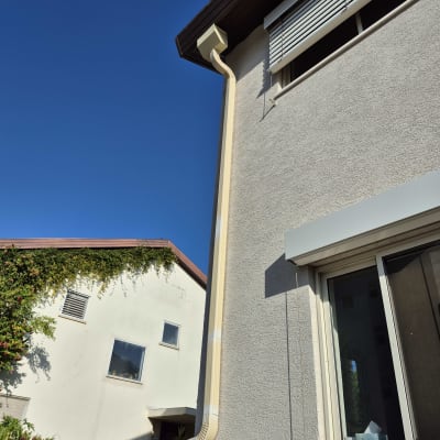 מרזב על קיר בית עם חלון ותריסים