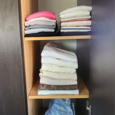 בגדים מקופלים בארון עץ כהה, מסודרים לפי צבעים