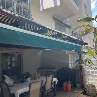 סוכך ירוק תלוי מעל מרפסת עם שולחן וכיסאות