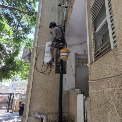 אדם עובד בגובה על קיר בניין עם ציוד בטיחות