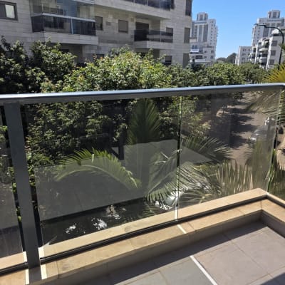 מעקה זכוכית במרפסת עם נוף לבניינים ועצים