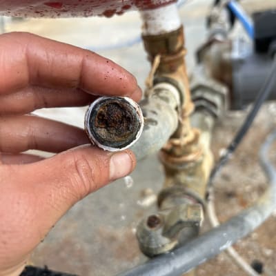 יד מחזיקה צינור חלוד עם אבנית, חלק ממערכת חימום מים.