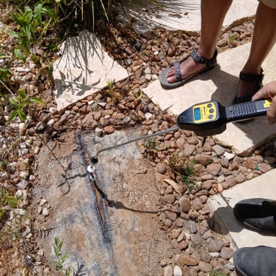 אדם מחזיק גלאי נזילות מעל קרקע עם אבנים