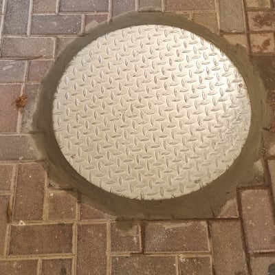 מכסה מתכת עגול על מדרכה מרוצפת בלבנים