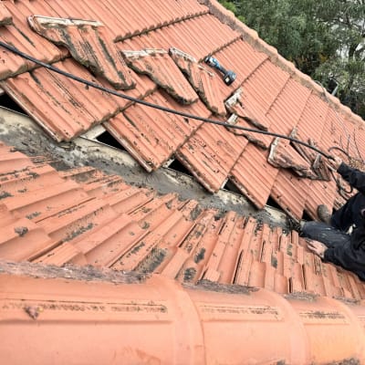 אדם מתקן רעפים על גג רעפים אדום