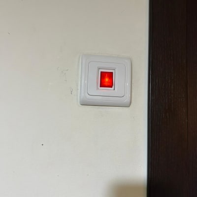 מתג חשמלי עם אור אדום דולק על קיר לבן