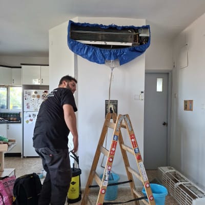 אדם עובד על מזגן עם סולם וכלים