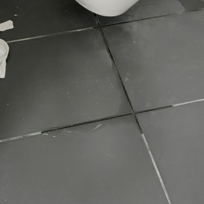 רצפת אריחים שחורים עם סימני רטיבות ליד אסלה