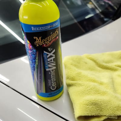 בקבוק ווקס קרמי ומטלית צהובה על מכסה רכב