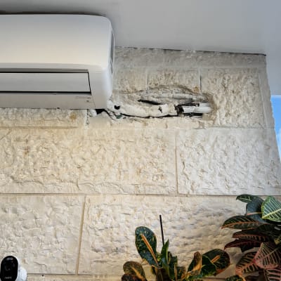 מזגן מותקן על קיר אבן עם צמחים לידו