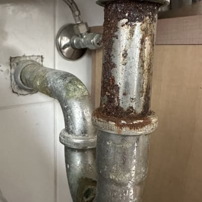 צינור מתכת חלוד מתחת לכיור עם חיבורים