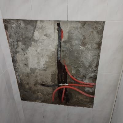 צינורות מים אדומים בקיר פתוח בחדר אמבטיה