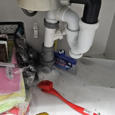 צנרת מתחת לכיור עם מברשת אדומה וחומרי ניקוי