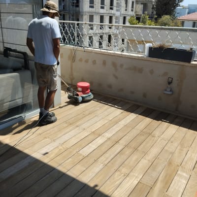 אדם משייף רצפת עץ במרפסת עם מכונה