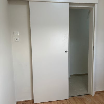 דלת הזזה לבנה עם ידית עגולה על רצפת עץ