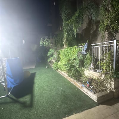 גינה פרטית בלילה עם דשא סינטטי, ערוגת צמחייה וכלי גיזום