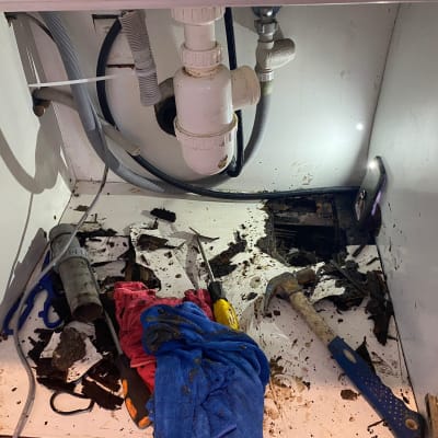 כלי עבודה מתחת לכיור, כולל פטיש ובגדים מלוכלכים
