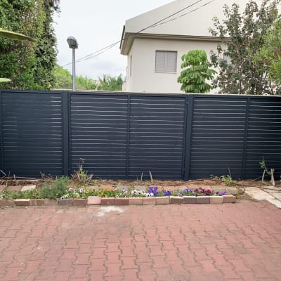 גדר אלומיניום אפורה בחצר עם צמחייה מסביב